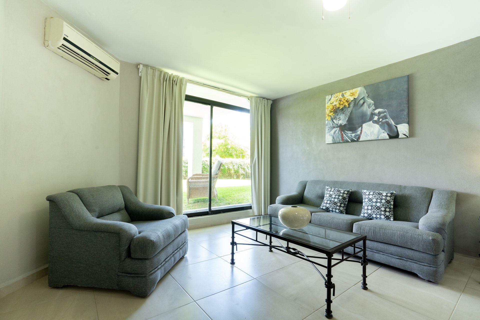 Sala de estar con muebles grises, ventana, mesa de café y obras de arte.