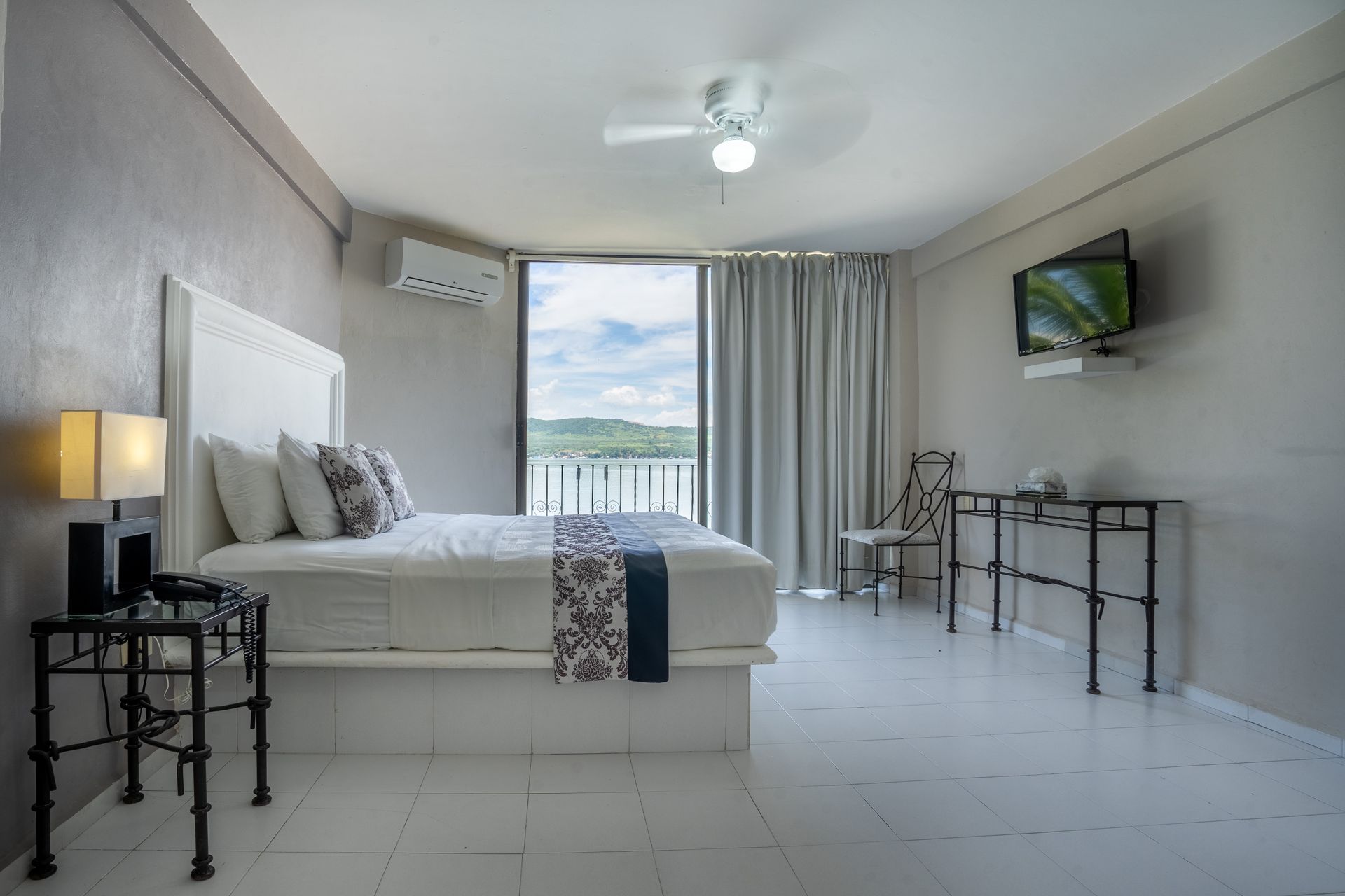 Dormitorio con cama, TV y vista al agua a través de grandes puertas.