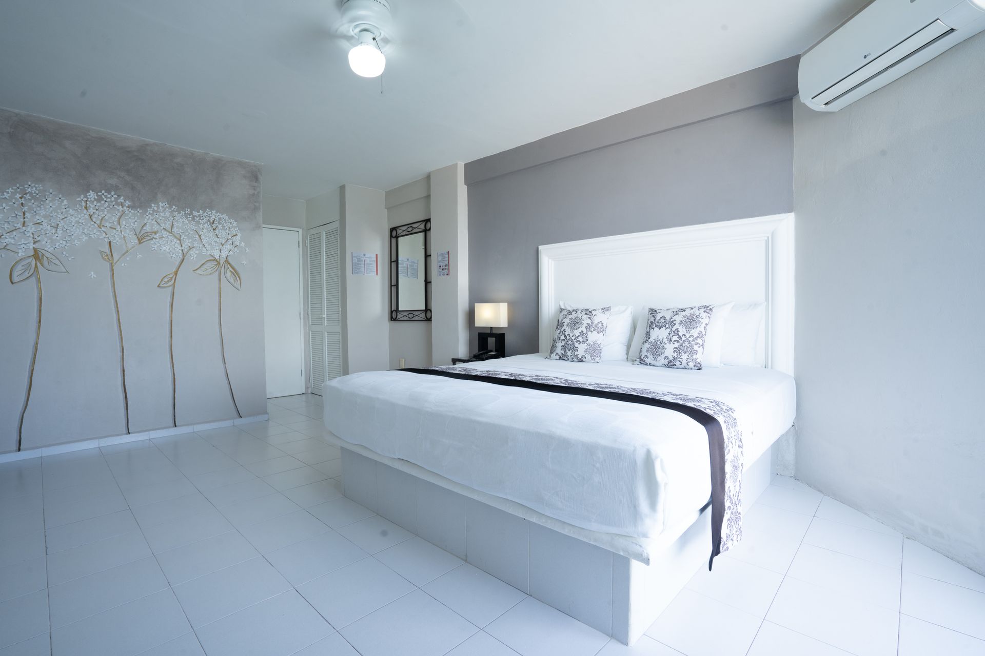 Dormitorio blanco con cama grande, pared decorativa y aire acondicionado.