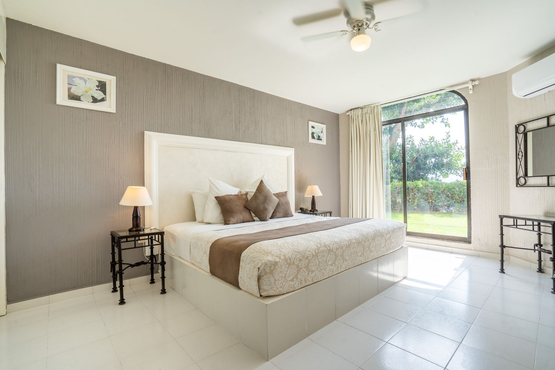 Dormitorio con cama blanca, pared con acento gris, puerta corrediza de vidrio y mesas auxiliares.