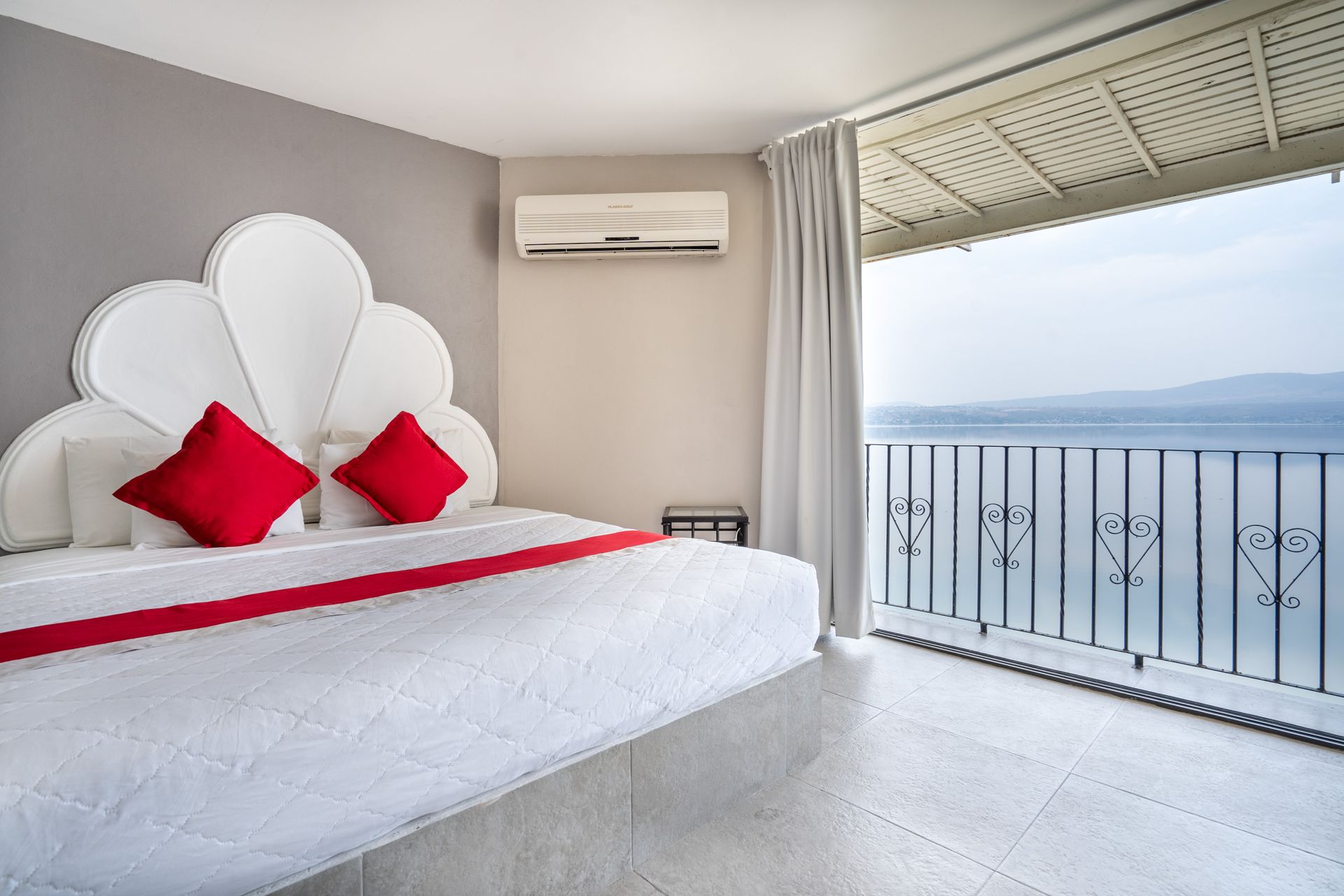Dormitorio con cama king-size, almohadas rojas, vista al mar desde el balcón y paredes grises.