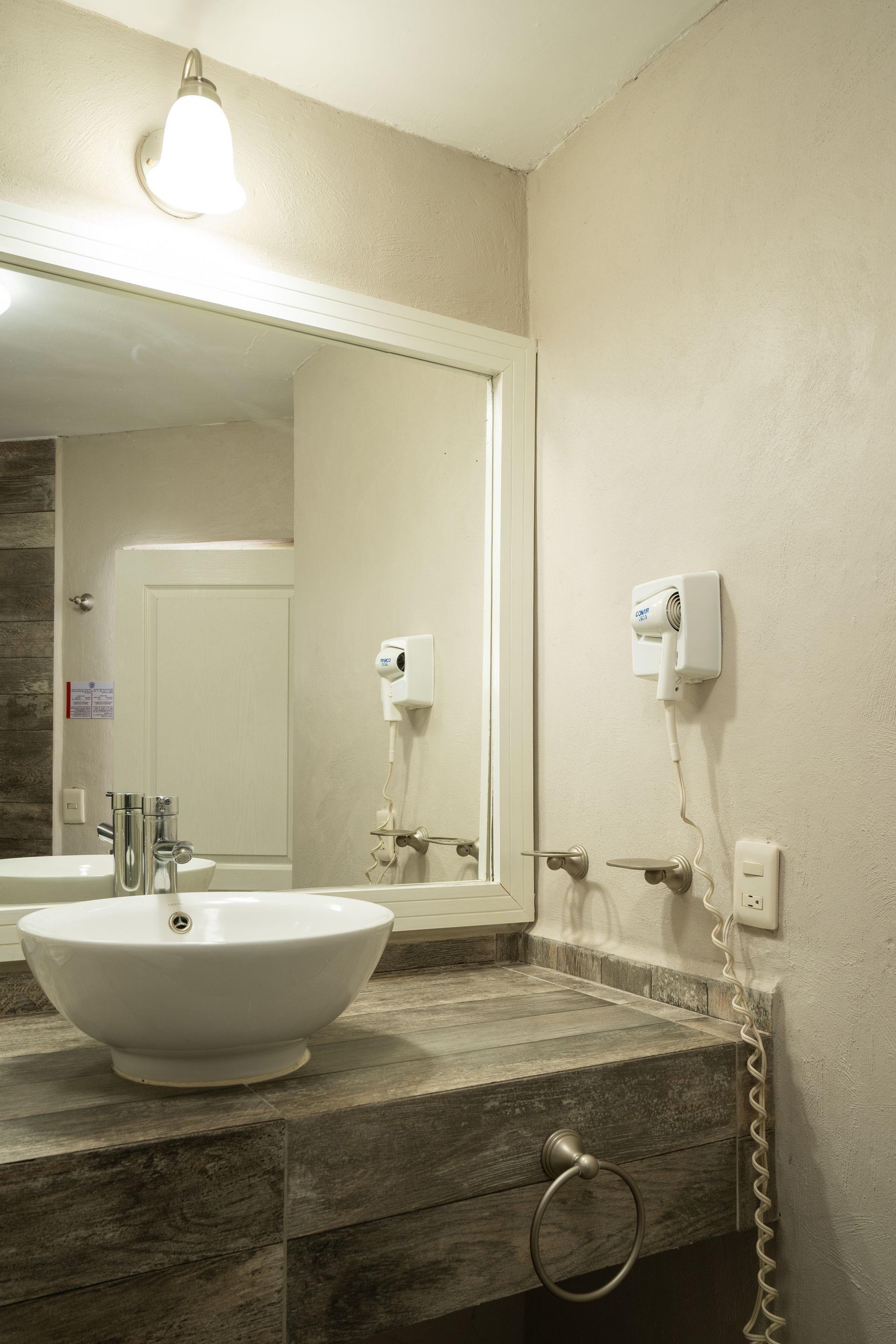 Mueble de baño con lavabo, espejo, secador de pelo y toallero; colores neutros.