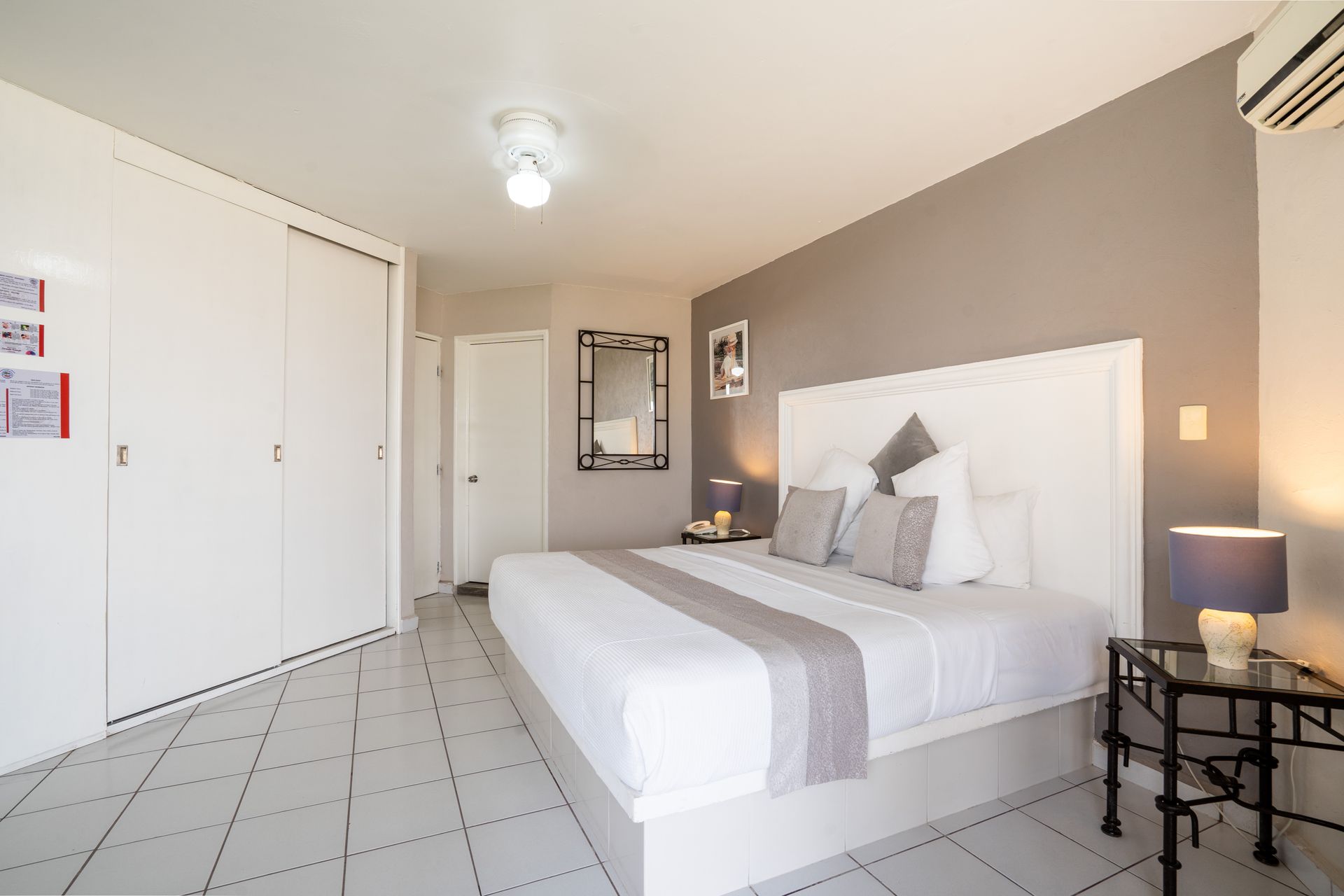 Dormitorio con cama blanca, pared con acento gris, armario blanco y piso de baldosas.