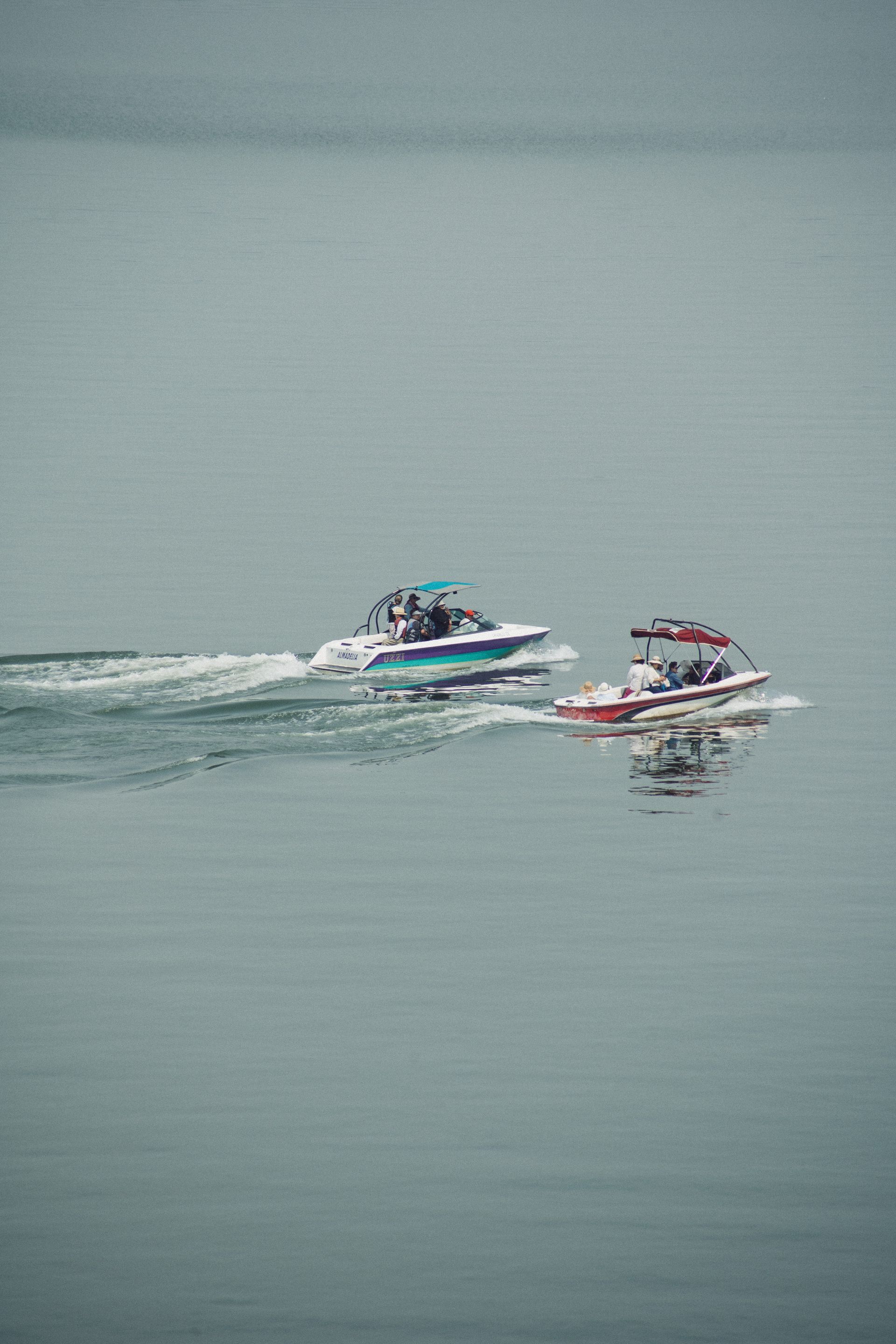 Dos lanchas en un lago tranquilo. La más grande es blanca y azul, la más pequeña es roja.