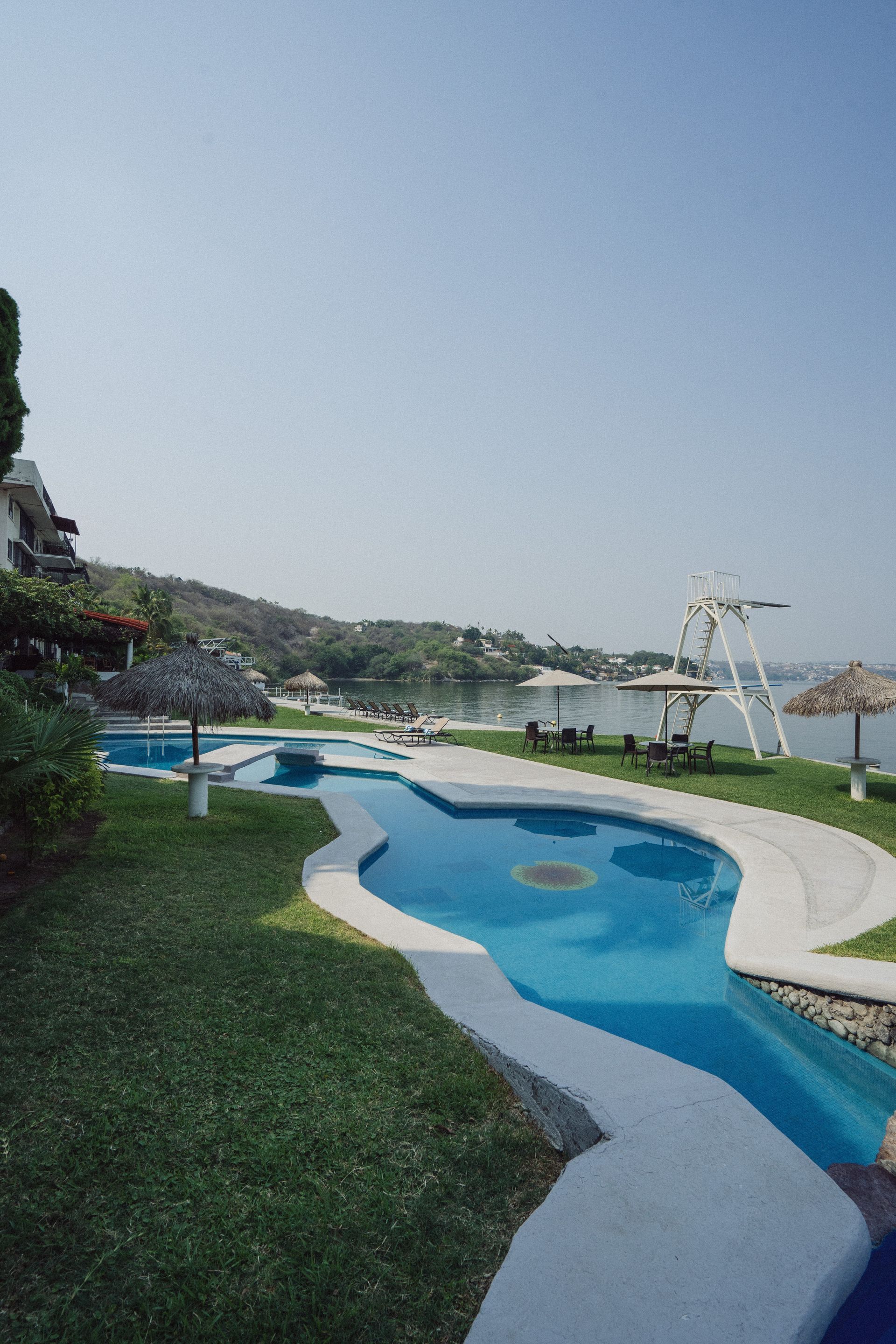 Una piscina larga y sinuosa sobre un césped junto a un lago.