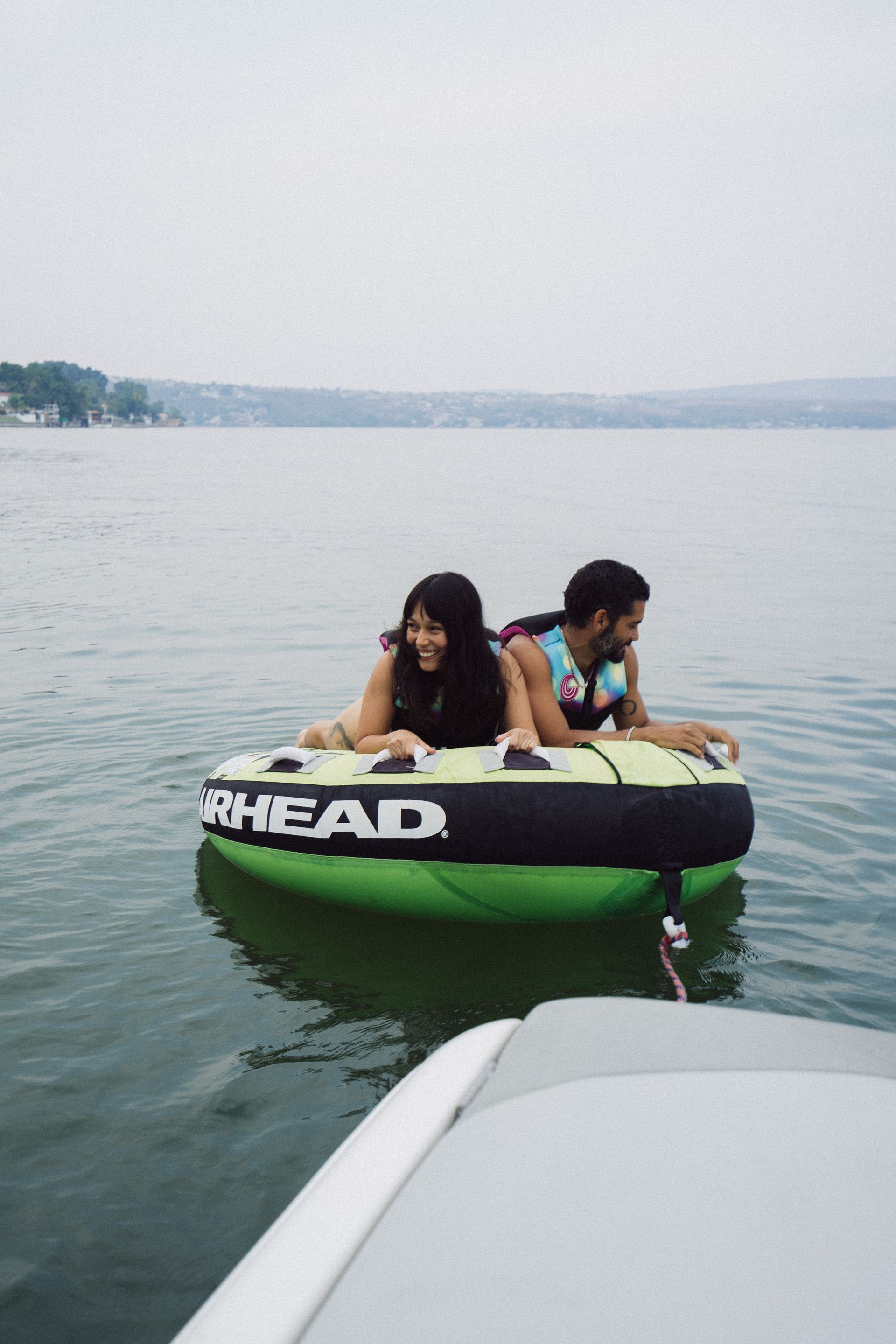 Dos personas en un tubo verde en el agua, sonriendo, siendo arrastrados por un bote.