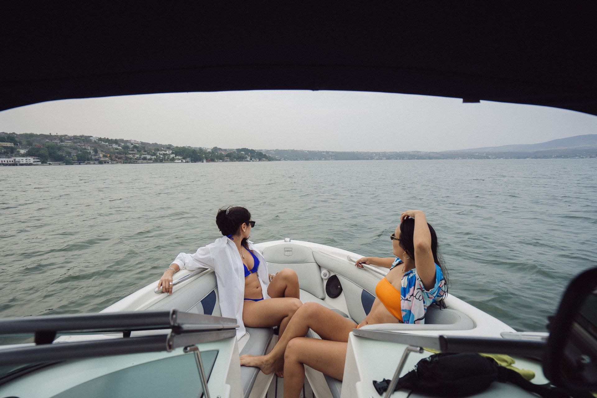Dos mujeres en bikini en un bote, mirando al horizonte. Una lleva una camisa blanca.
