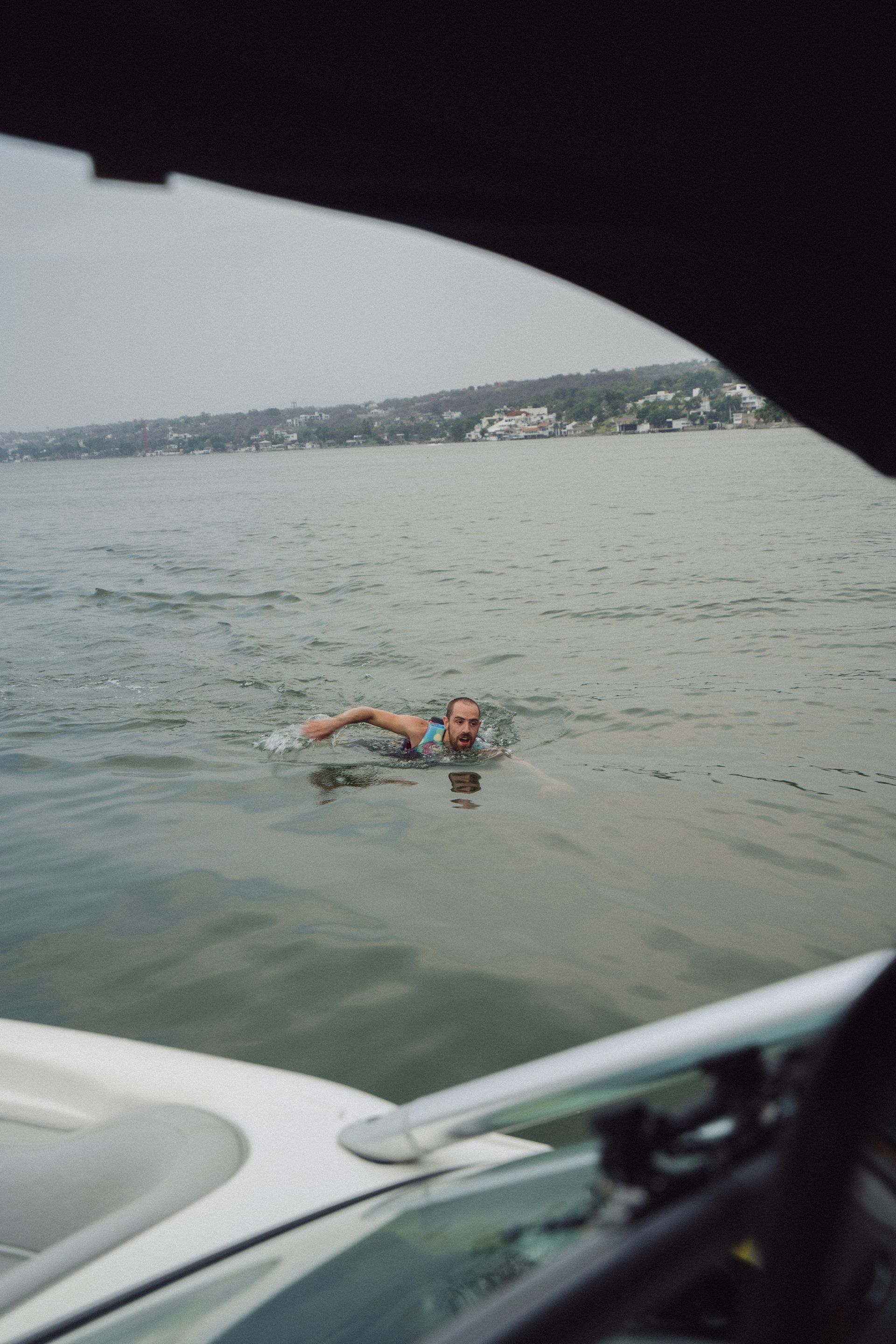 Persona nadando en un cuerpo de agua, vista desde el interior de un bote en un día nublado.