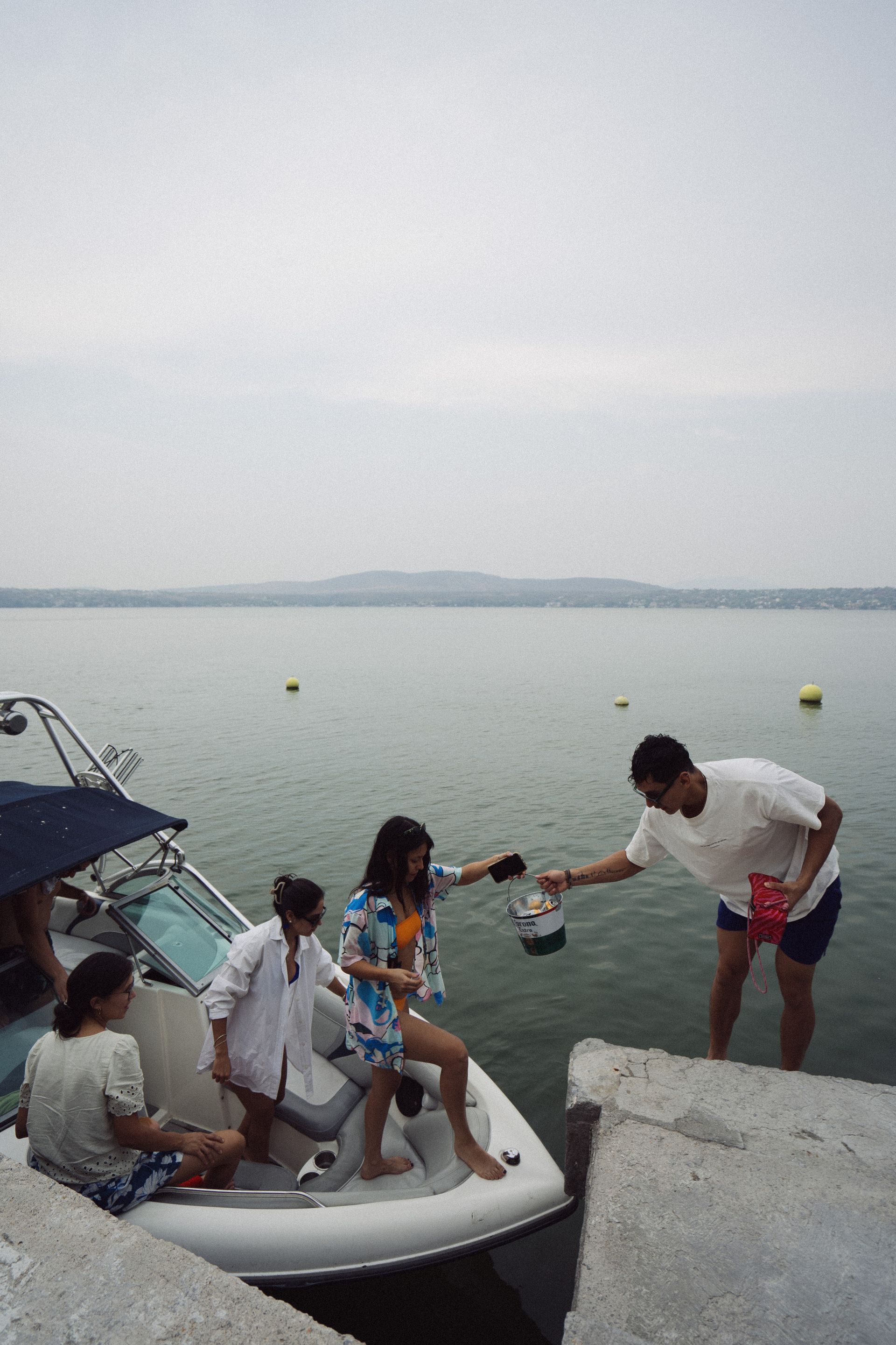 Personas en un barco recibiendo algo de un hombre en un muelle en un lago.