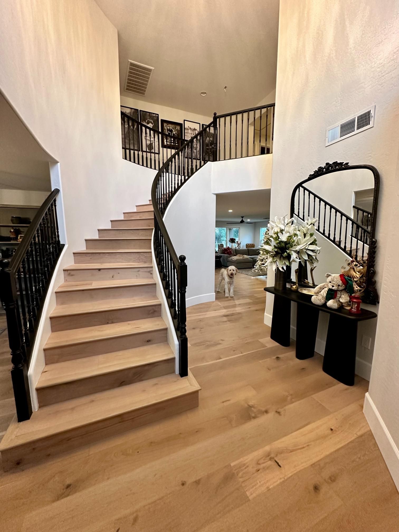 Wooden staircase with black railing, leading to an upper level. Foyer with large mirror and table.