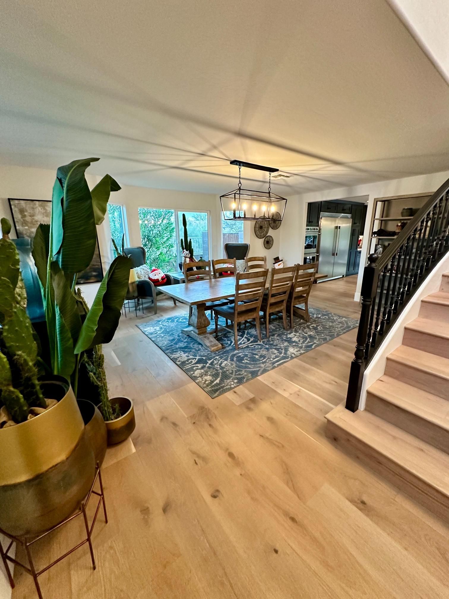 Spacious dining room with wooden floor, table, and chairs; plants in foreground; stairs on right.