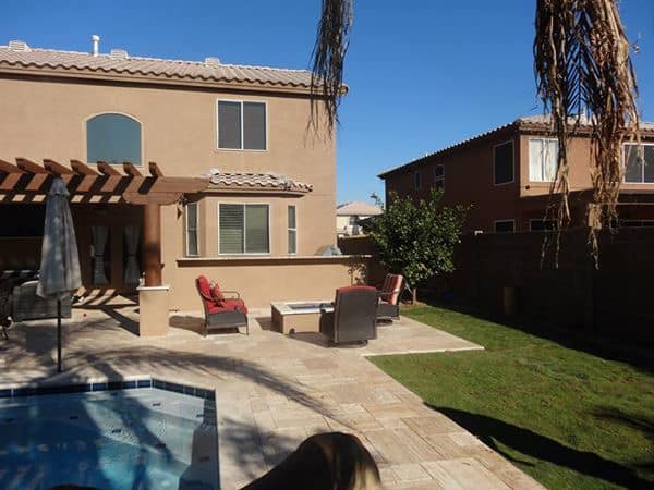Backyard with pool, patio, seating, and two-story houses under a sunny sky.