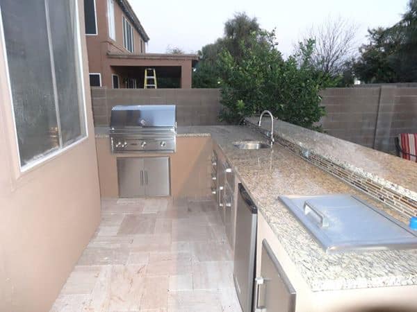 Outdoor kitchen with a stainless steel grill, sink, and countertops.