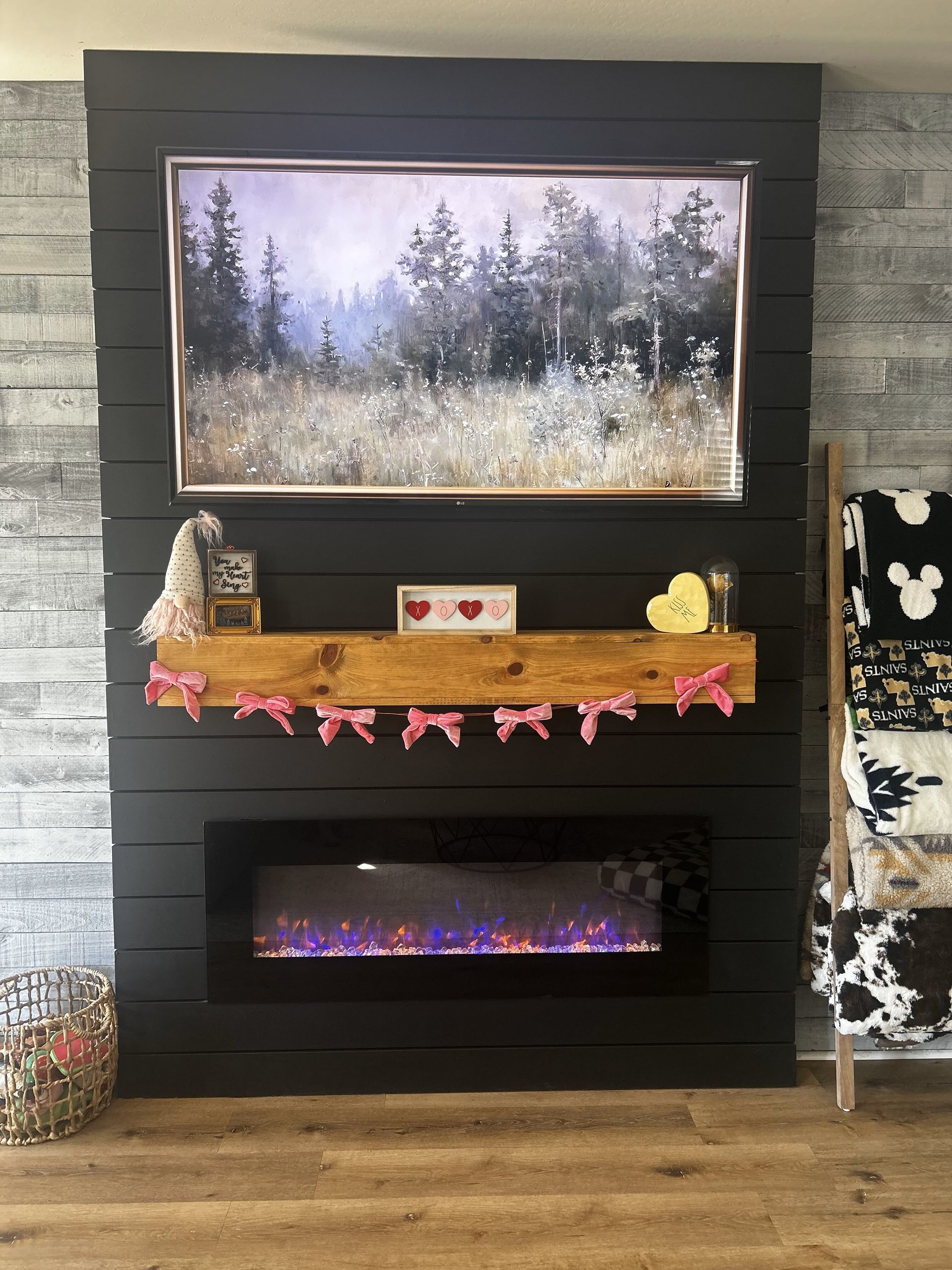 Fireplace with framed artwork of a forest, a wooden mantel decorated with pink bows, and an electric fire.