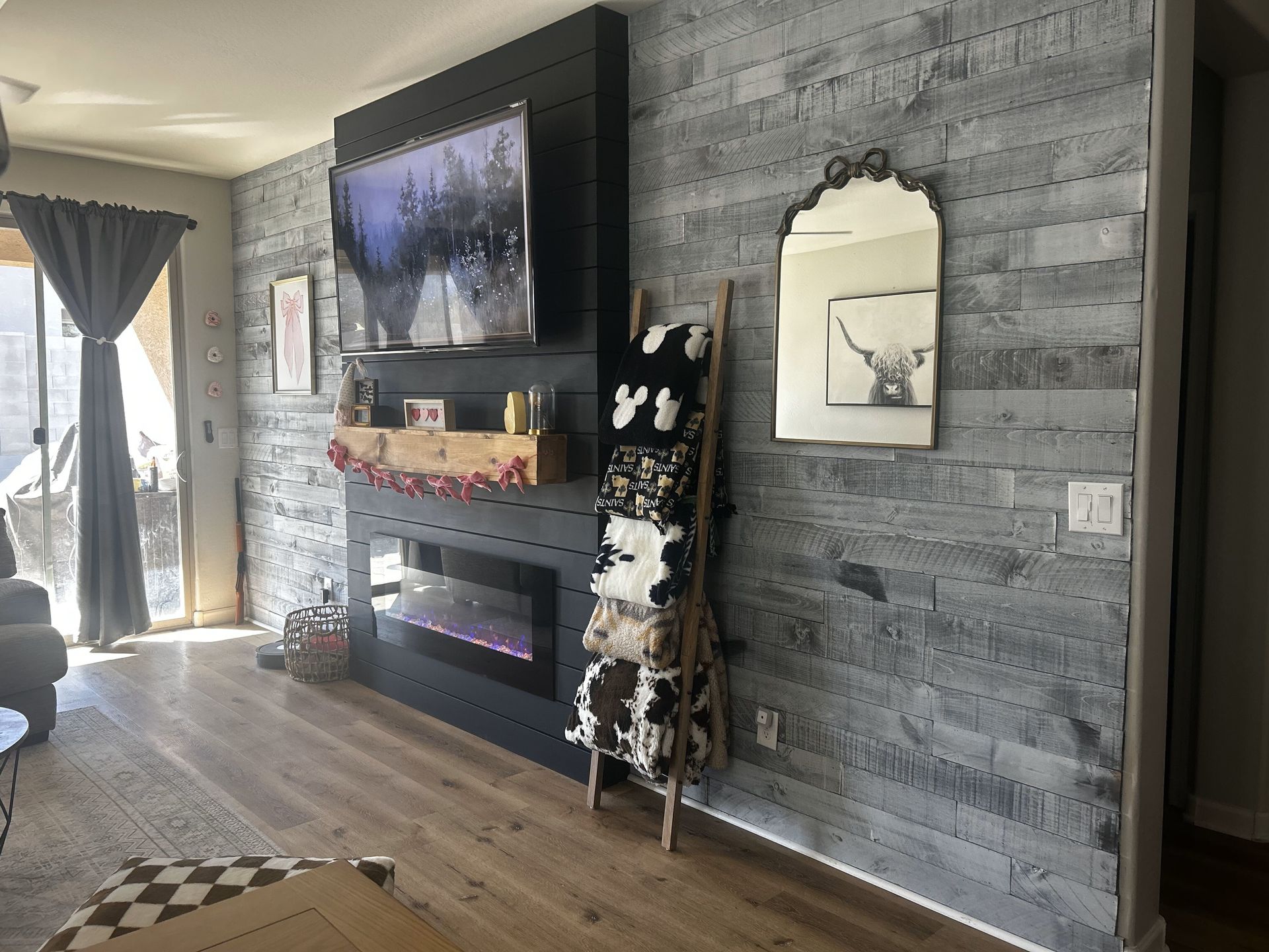 Living room with gray wood-look accent wall, fireplace, TV, blanket ladder, and decorative mirror.