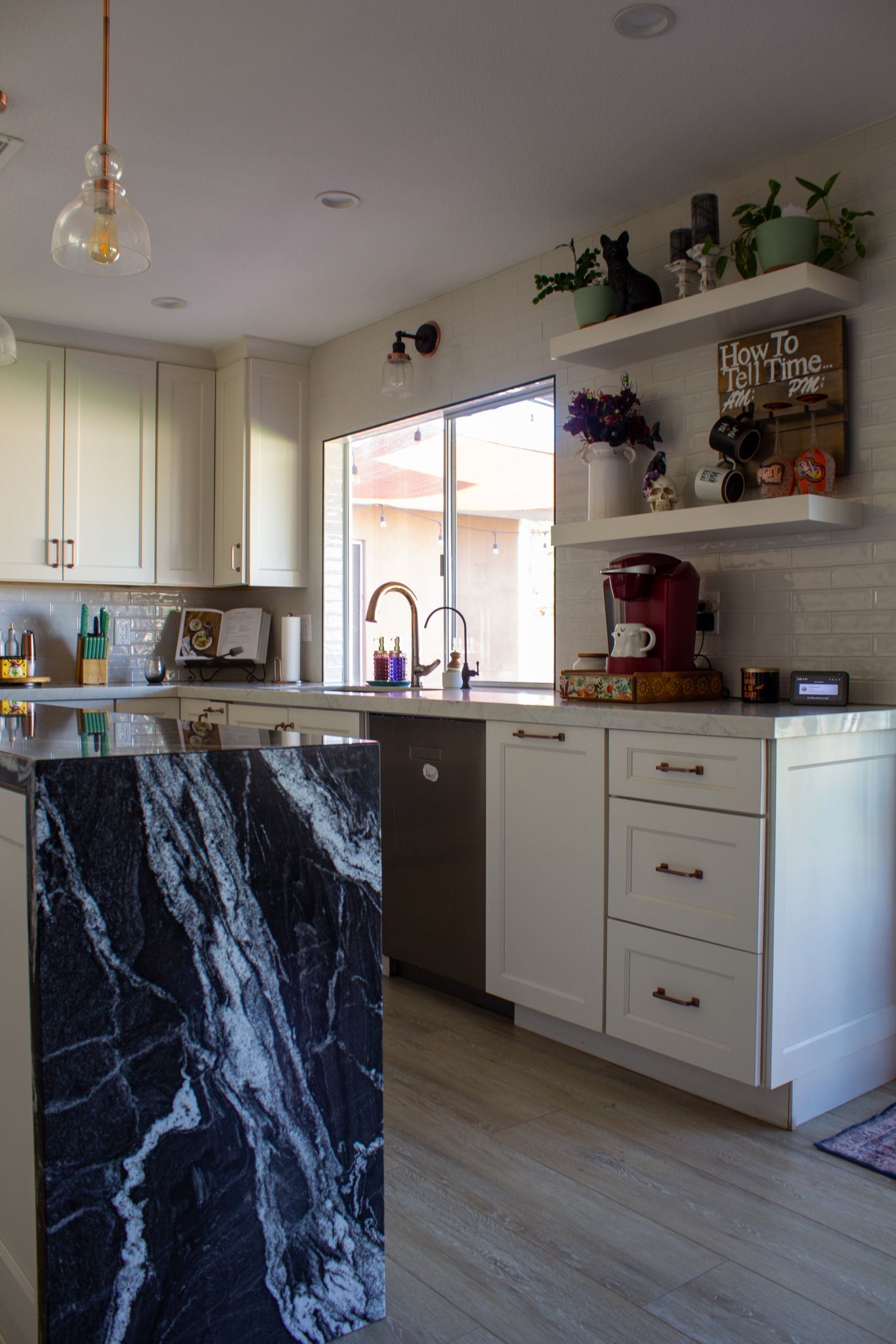 Kitchen with white cabinets, black marble island, shelves with plants, and a window.