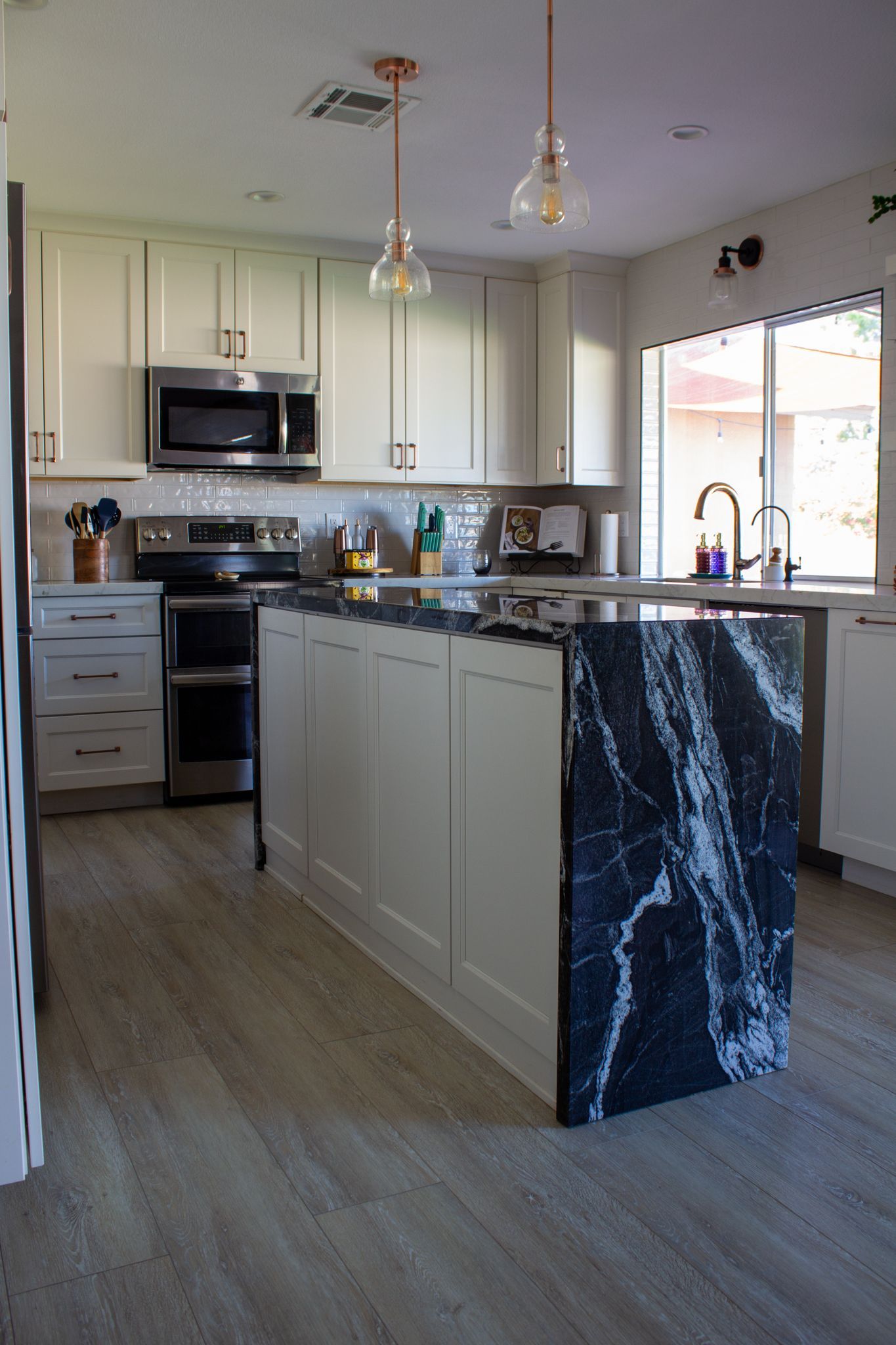 Kitchen with white cabinets, dark island countertop, and wood-look flooring.