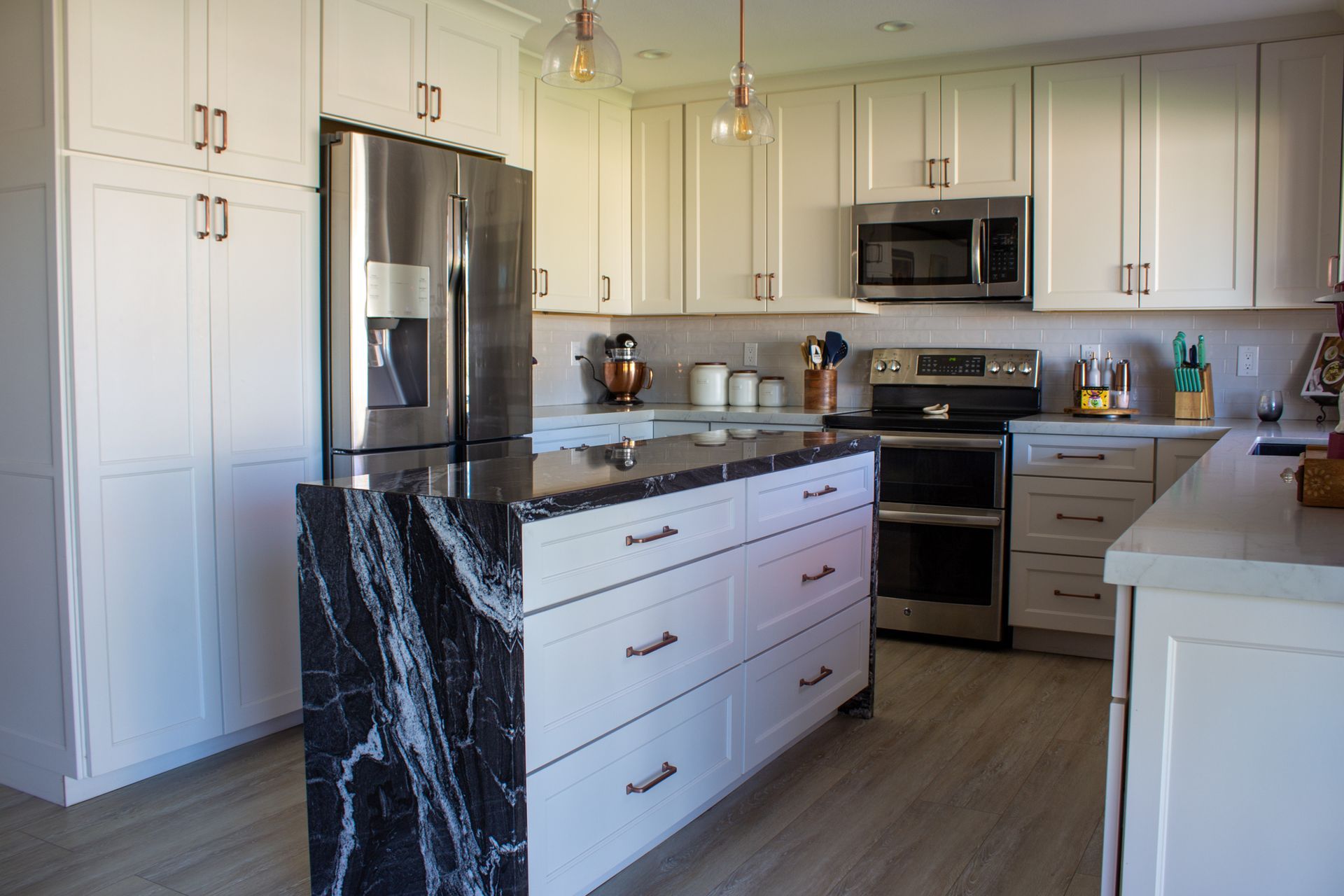 White kitchen with black marble island, stainless steel appliances, and copper hardware.