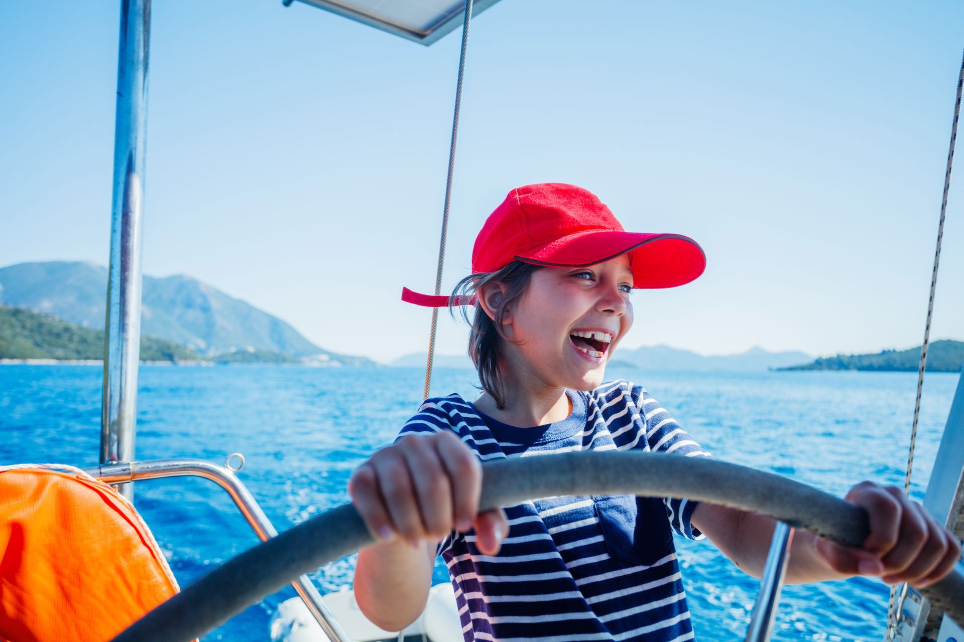 A young boy is steering a sailboat in the ocean.