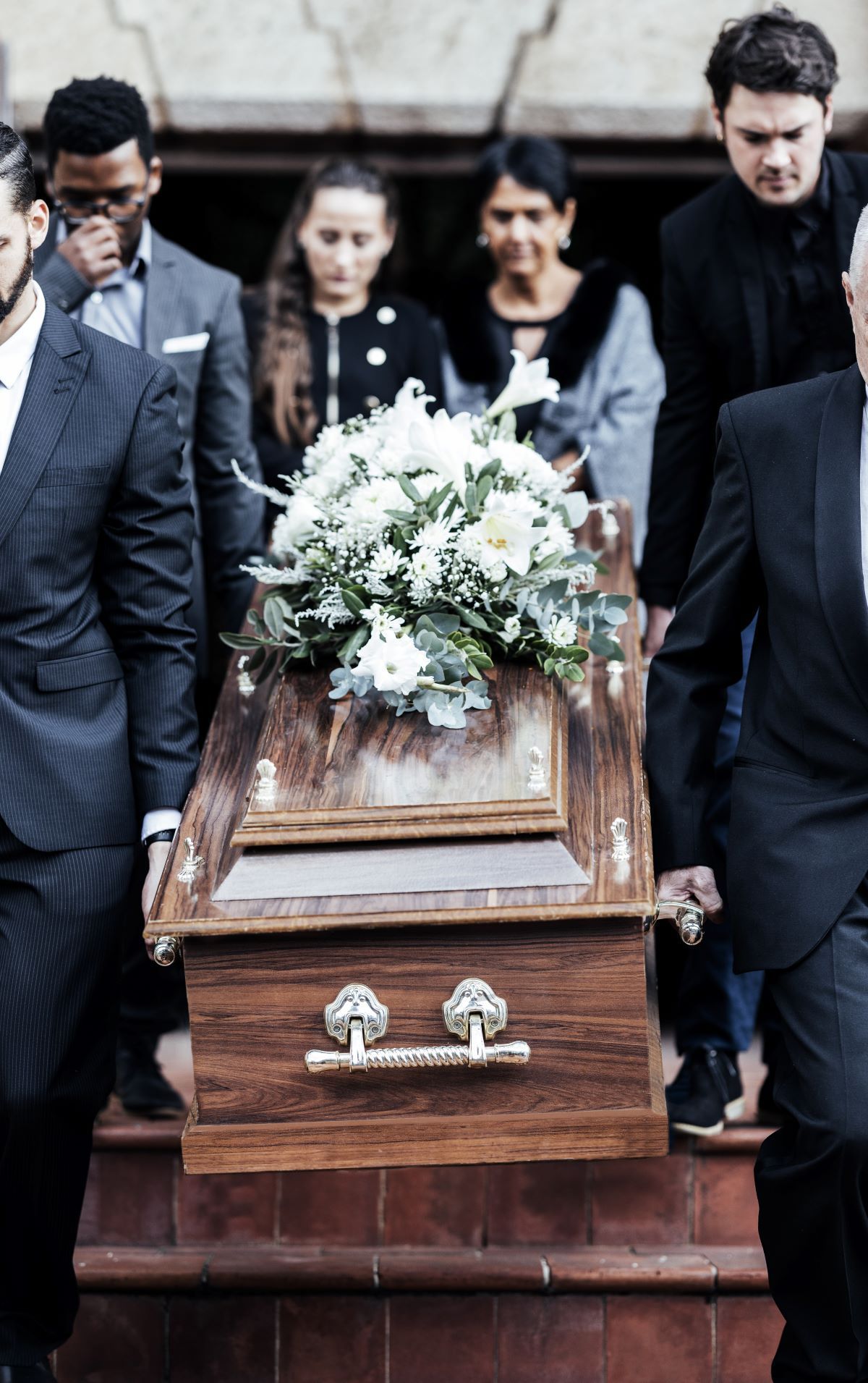 Mourners carry a wooden casket with white flowers at a funeral procession