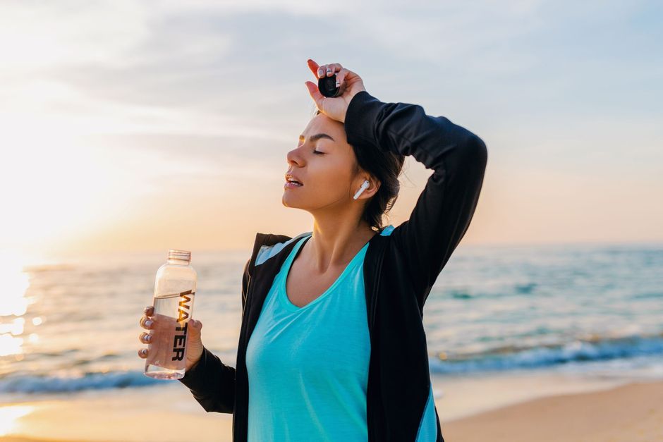 A woman is holding a bottle of water on the beach.