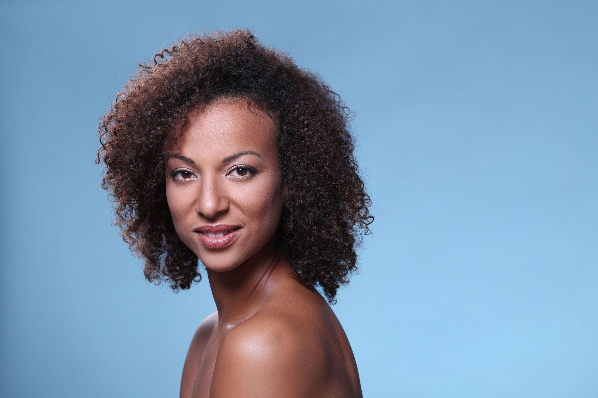 A woman with curly hair is looking over her shoulder at the camera.