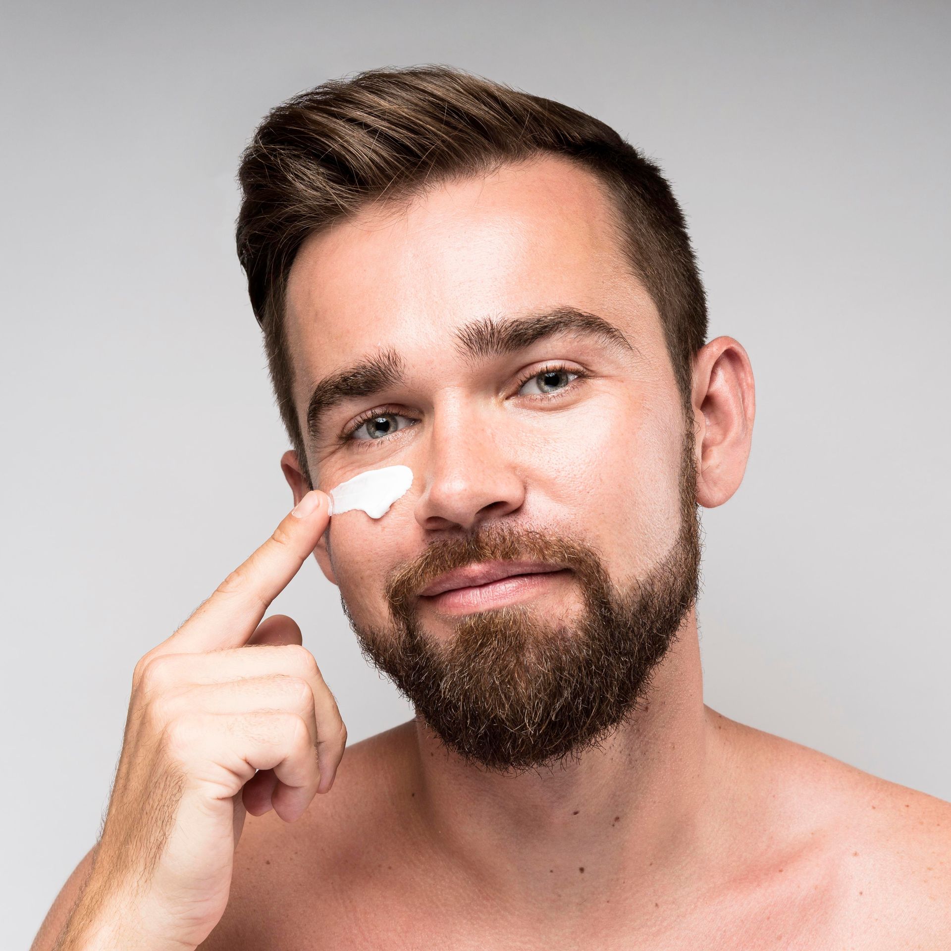 A man with a beard is applying cream to his face.