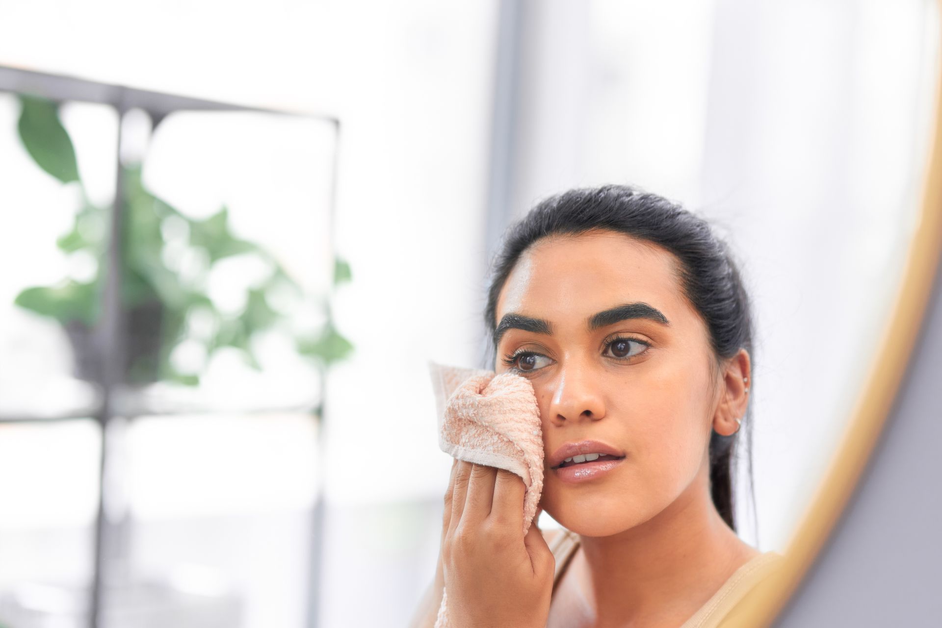 A woman is cleaning her face with a towel in front of a mirror.