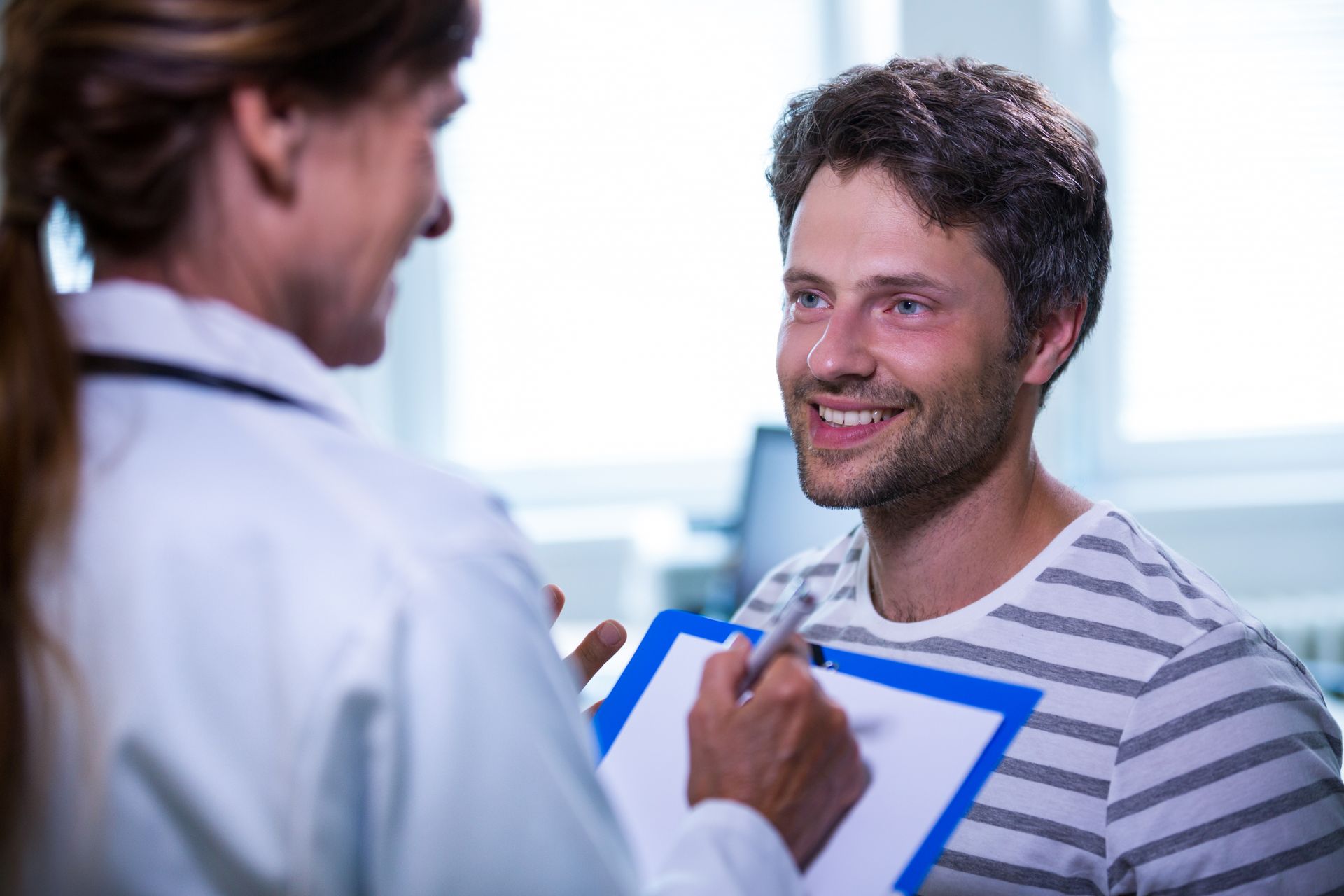 A doctor is talking to a patient who is smiling while holding a clipboard.