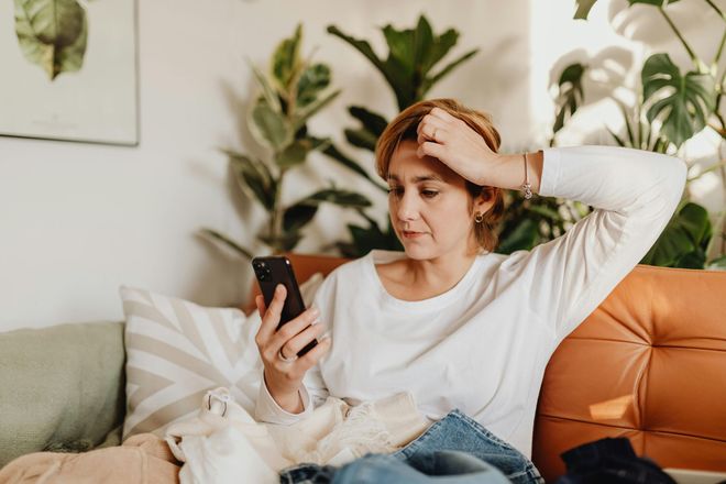 A woman is sitting on a couch looking at her cell phone.