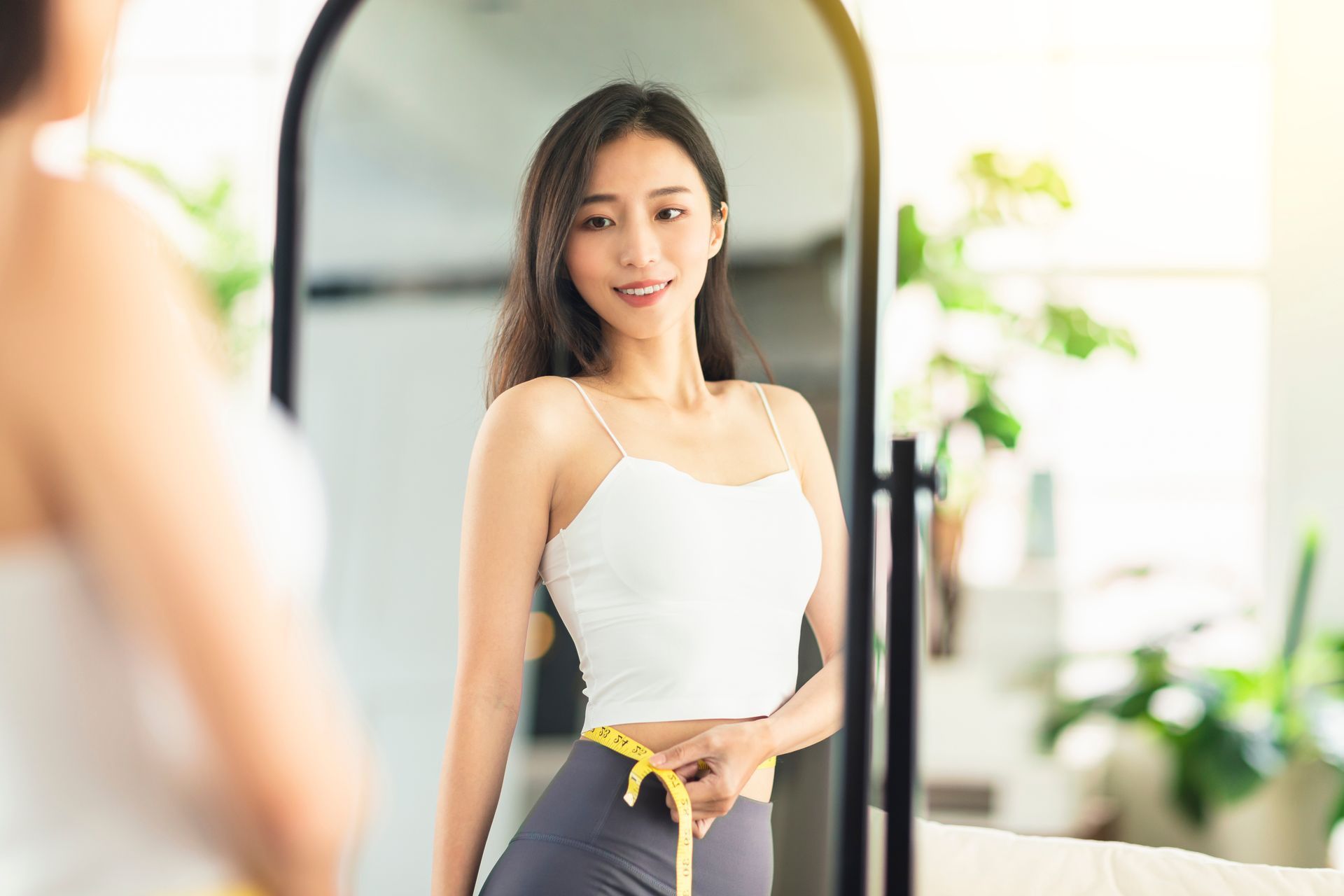 A woman is measuring her waist in front of a mirror.