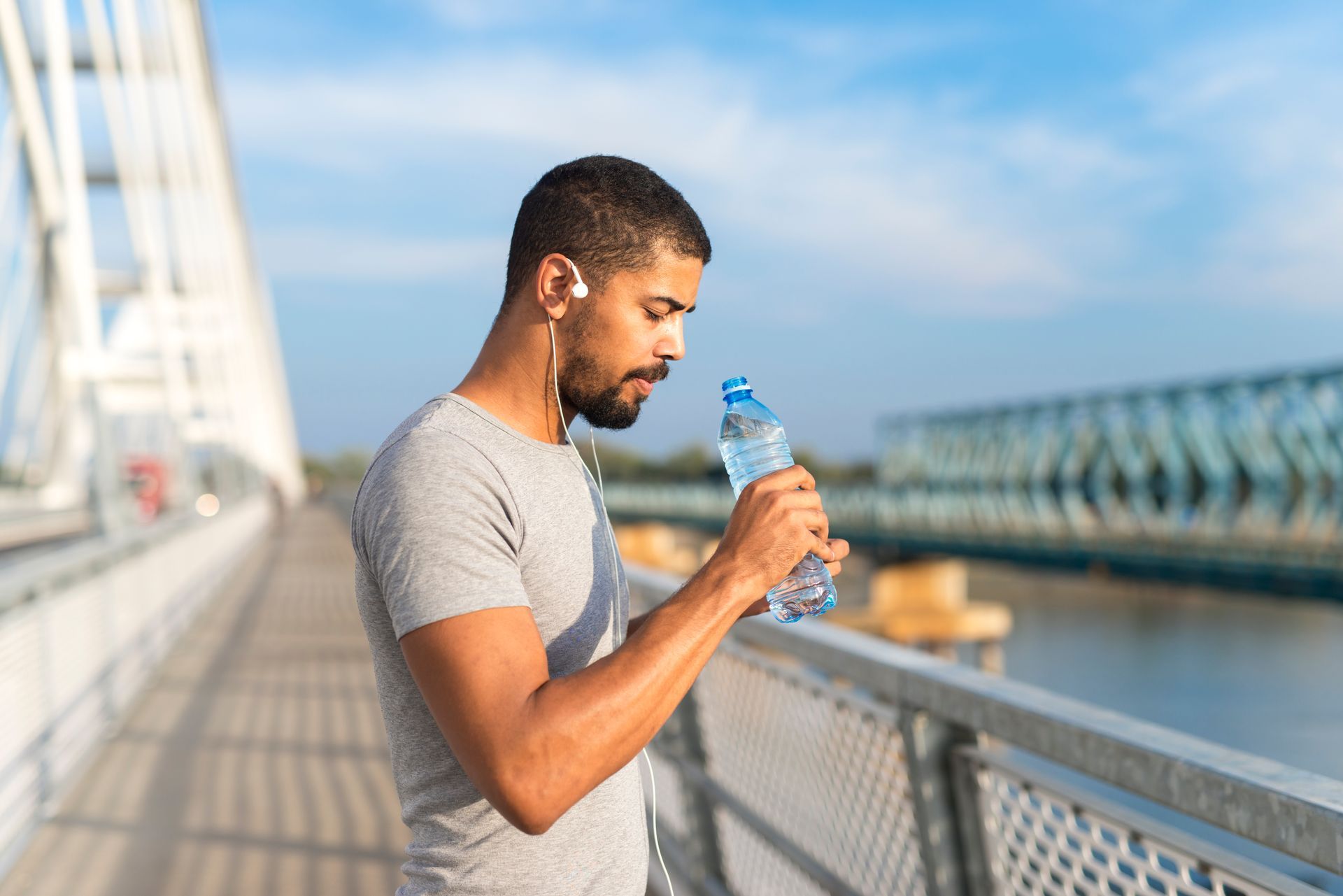 A man is drinking water from a bottle on a bridge.