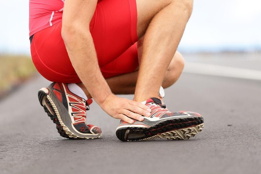 Runner crouched, holding ankle on road. Red shorts, athletic shoes, pained expression.