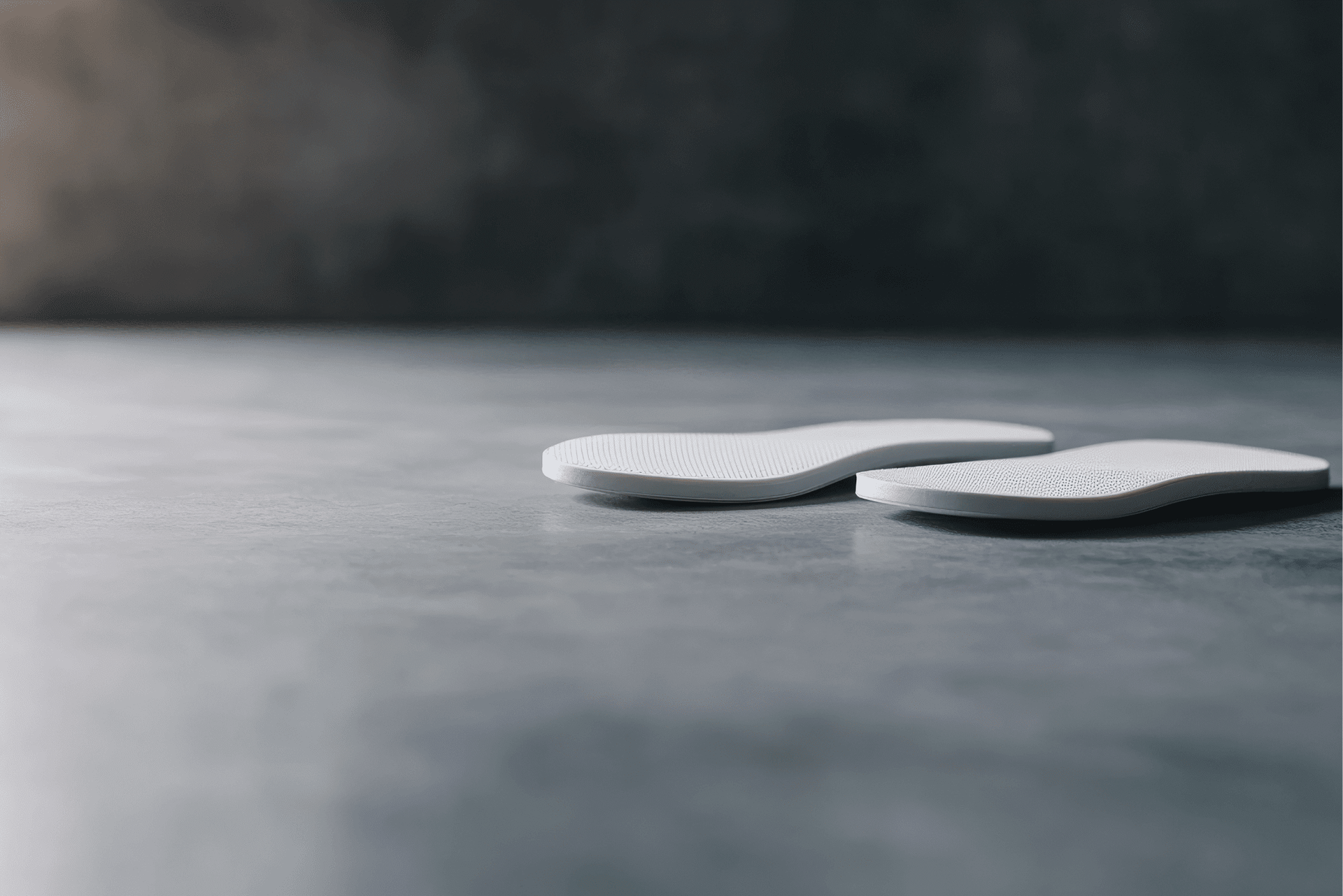 Two white shoe insoles on a gray concrete surface, with a dark, blurred background.