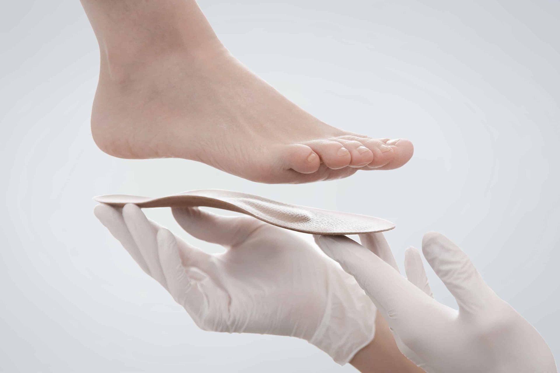 Foot hovering above an orthotic in gloved hands.