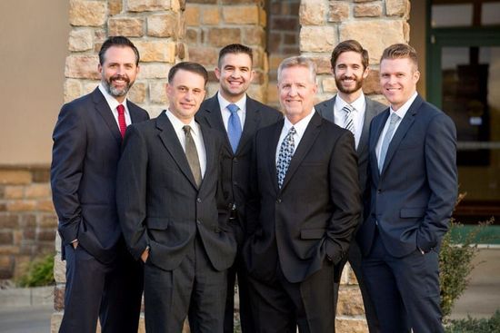 Six men in suits, smiling, posing in front of a stone building.