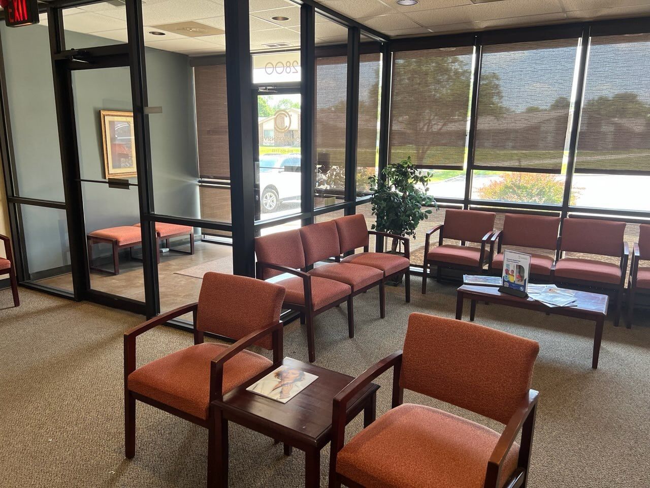 A waiting room with orange chairs, small tables, and large windows.
