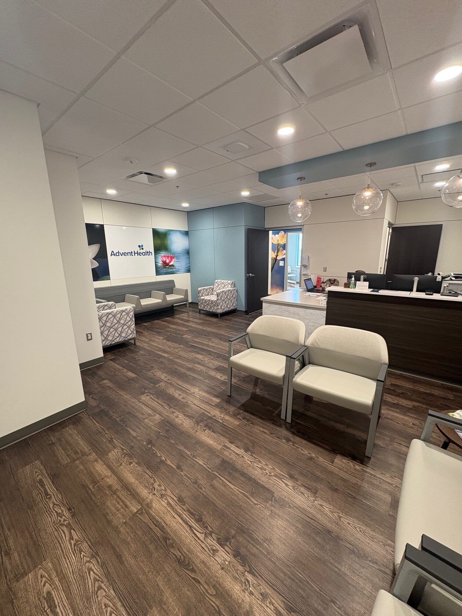 Waiting room with chairs, sofas, reception desk, and dark wood flooring.