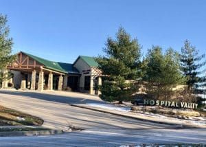 Hospital Valley entrance on a sunny day. Building has green roof, stone pillars, and a sign.