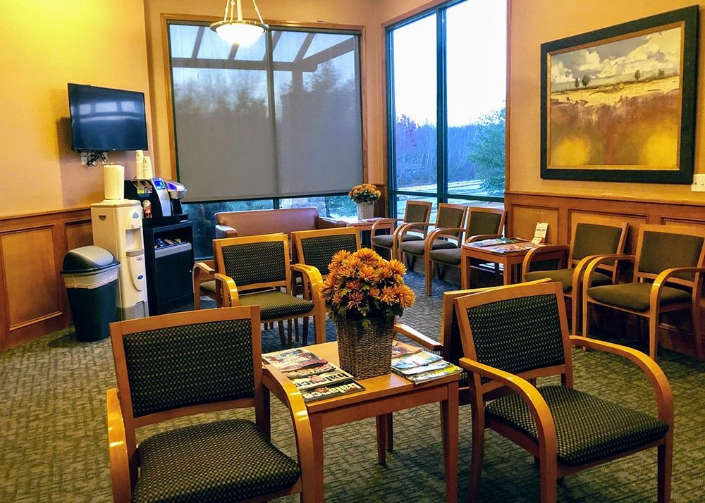 Waiting room with chairs, a small table with magazines, a beverage station, and a painting on the wall.