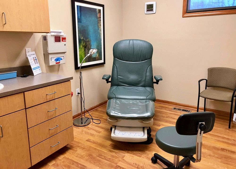 Podiatrist's examination room: green medical chair, neutral walls, framed art, and wooden cabinets.