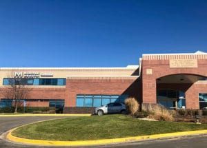 Hospital building with a red brick facade, blue windows, and a silver car.