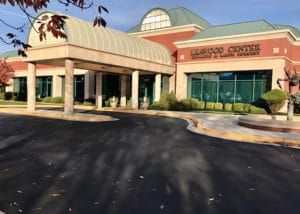 Building entrance: Larchwood Centre, red brick exterior, glass windows, arched entryway, overcast sky.