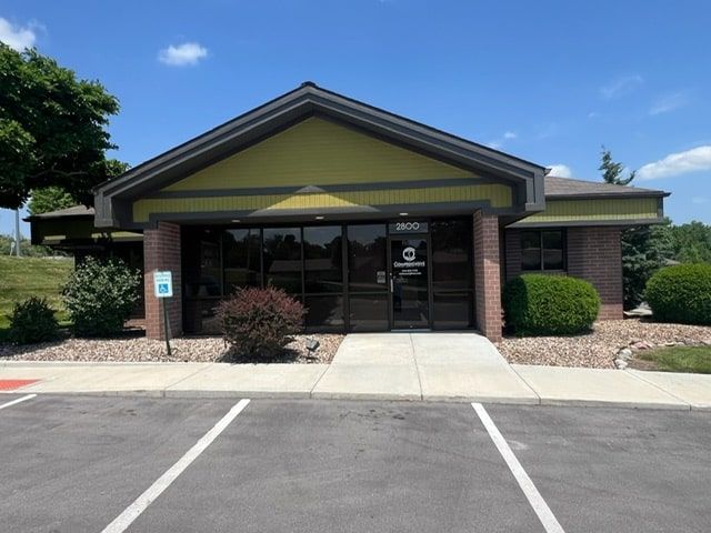 Exterior view of a one-story brick building with a dark glass front and a small parking lot.