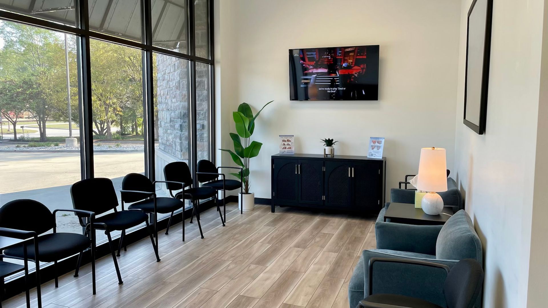 Waiting room with black chairs, a tv, and a large window.