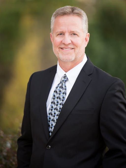 Man in suit and tie smiling outdoors.