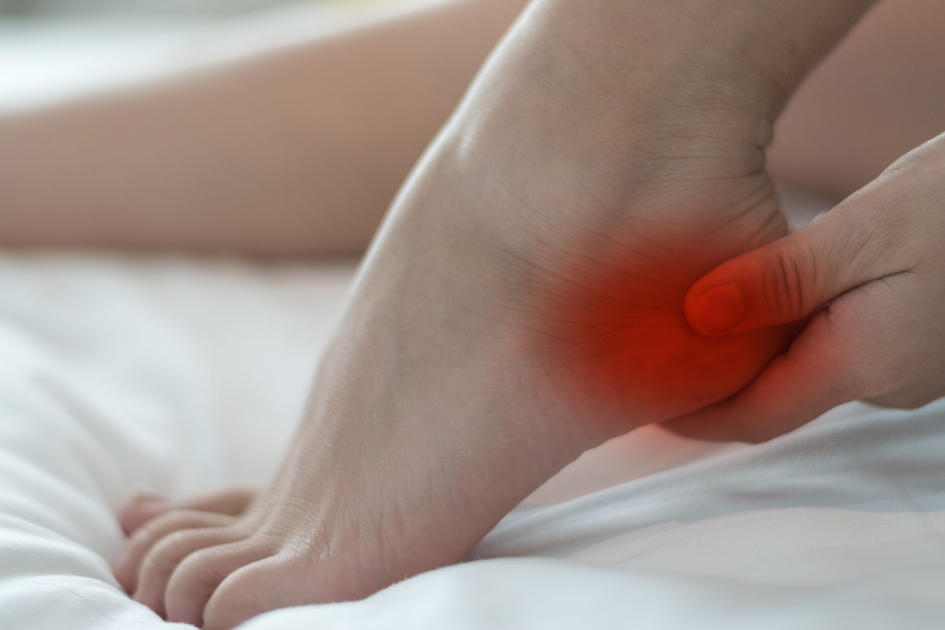 Foot with heel highlighted red, being held by a hand; likely experiencing pain.