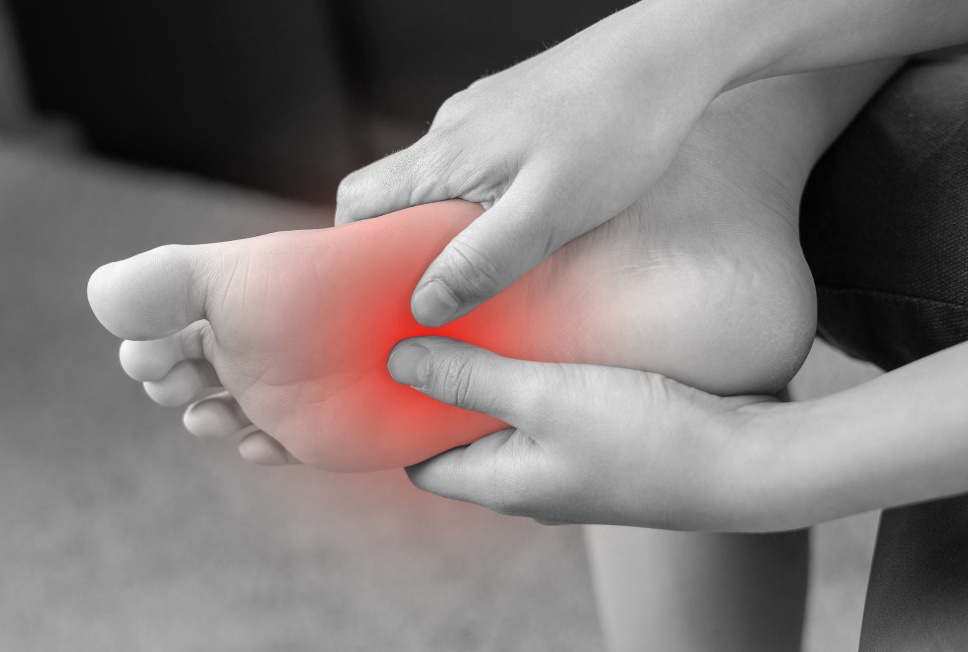 A person's foot is held by two hands, with the sole highlighted in red indicating pain.