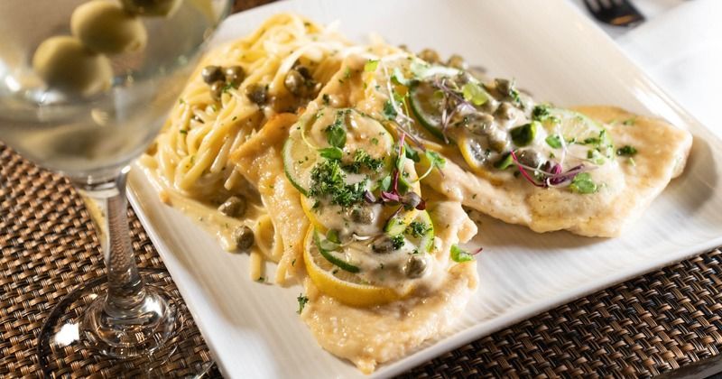 A white plate topped with chicken and noodles next to a martini glass.