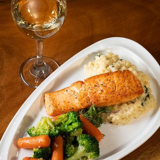 A plate of food with broccoli and carrots next to a glass of wine